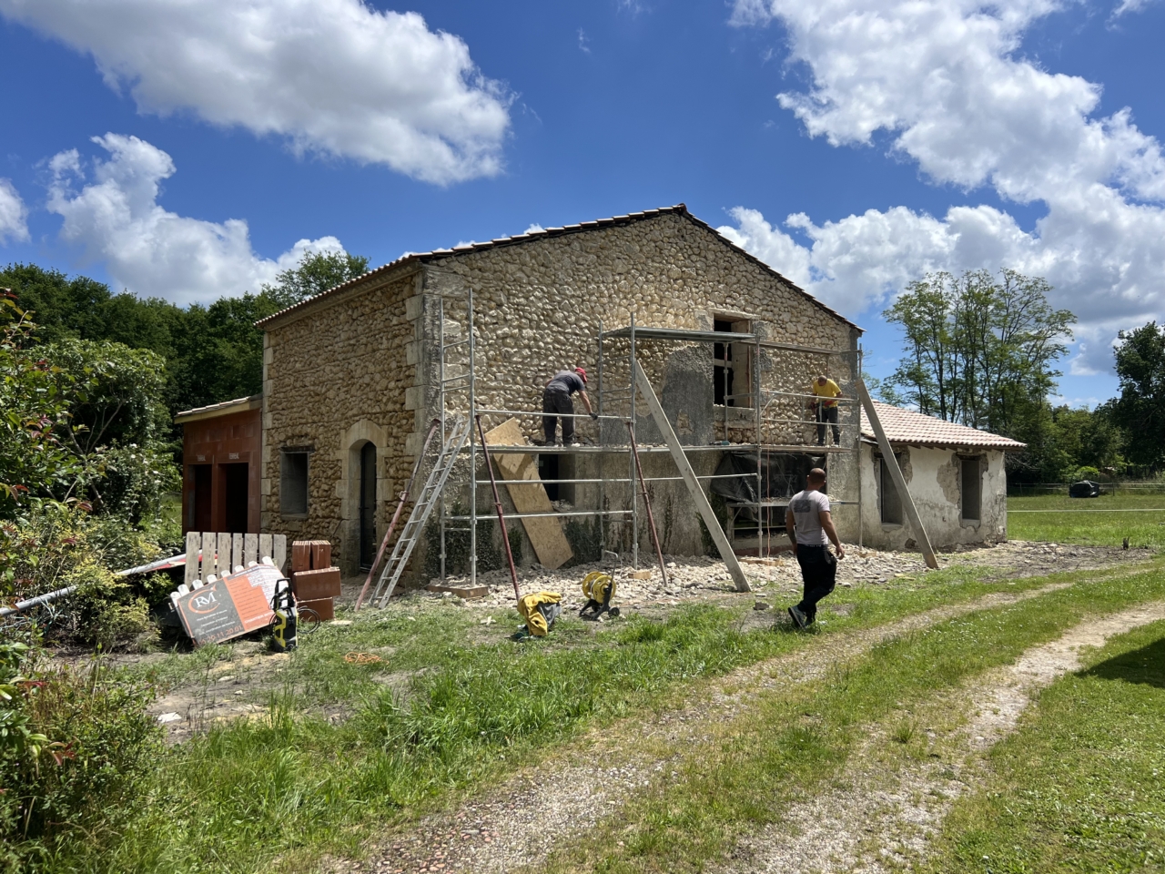 Rénovation et ravalement de la façade en pierre de la grange, avec échafaudage et artisans pendant les travaux de rénovation.