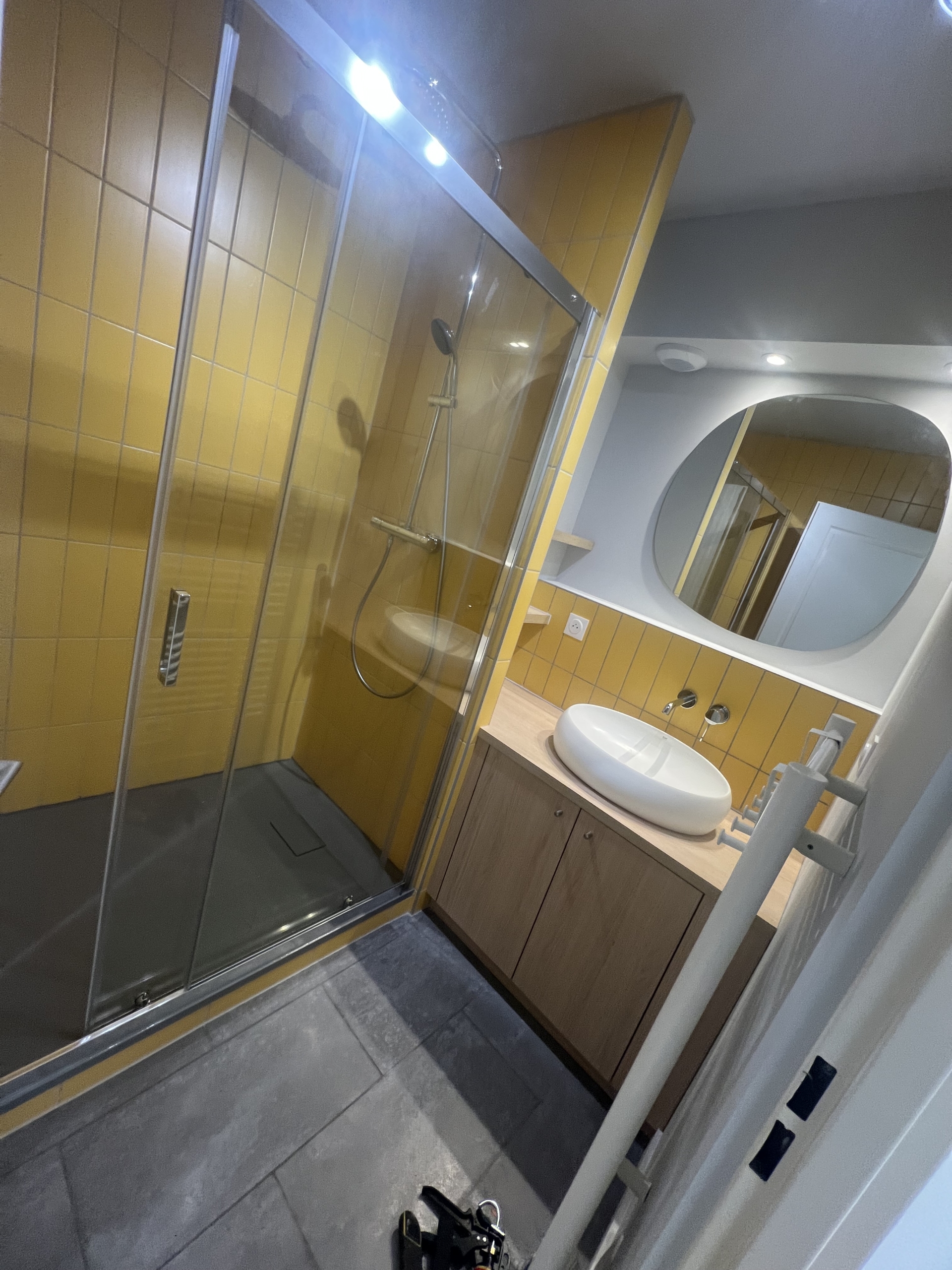 Salle de bain rénovée à Bordeaux avec douche vitrée, meuble vasque sur mesure en bois et carrelage jaune.